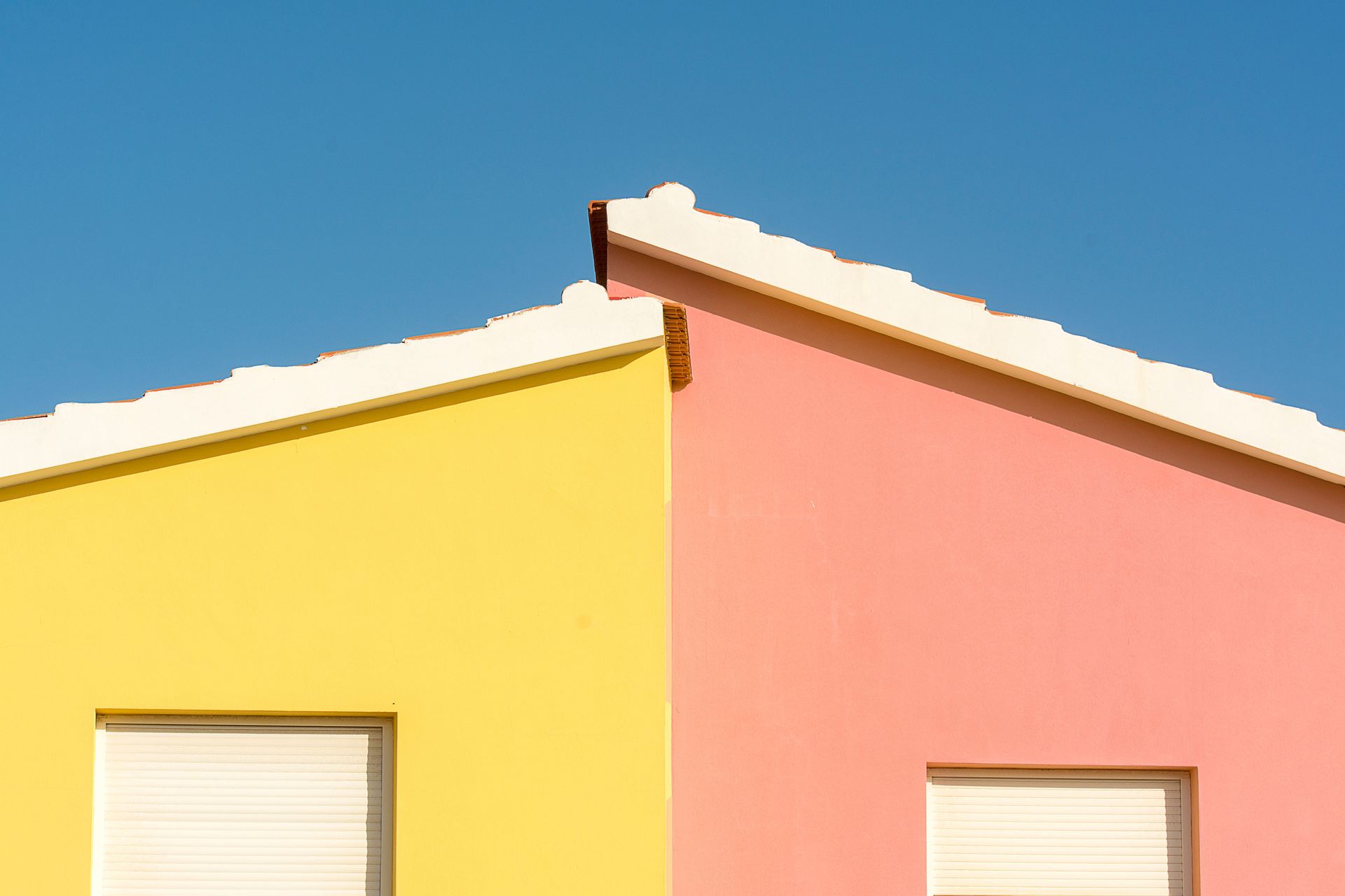 Close-up of vibrant yellow and pink house facades under a clear blue sky.